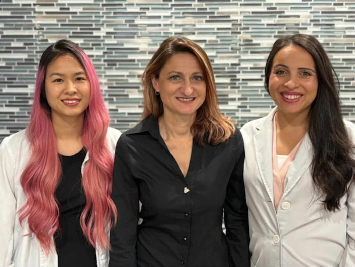Three friendly Simply Smiles clinicians, including Dr. Kira Gekht, smiling together at the practice
