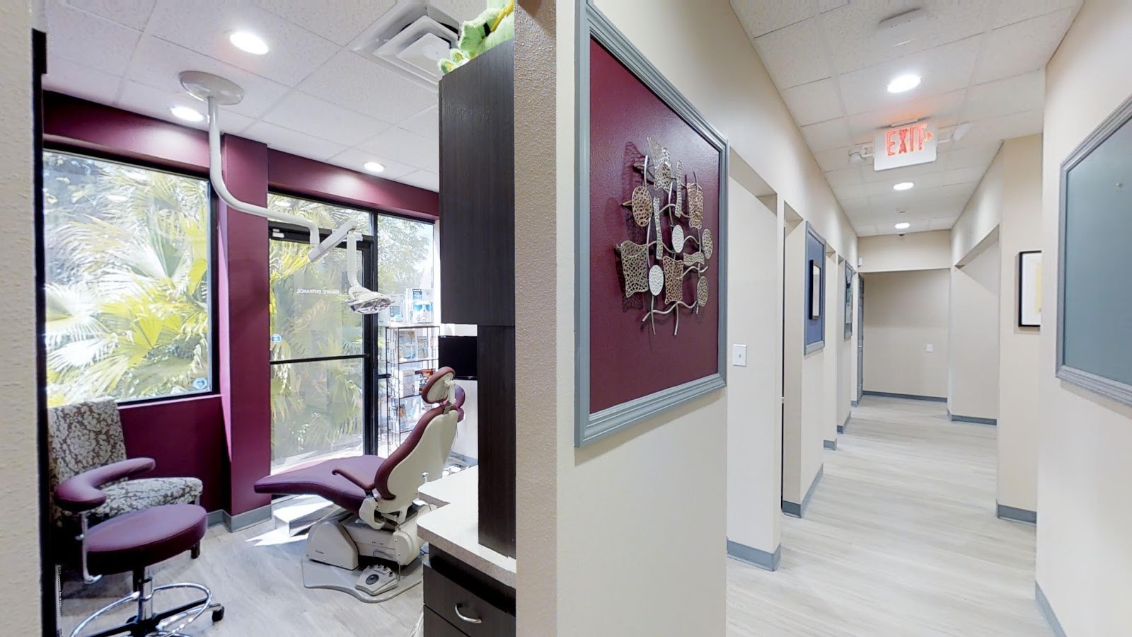 A bright treatment room at Simply Smiles with a burgundy accent wall and a window looking out onto Florida palm trees