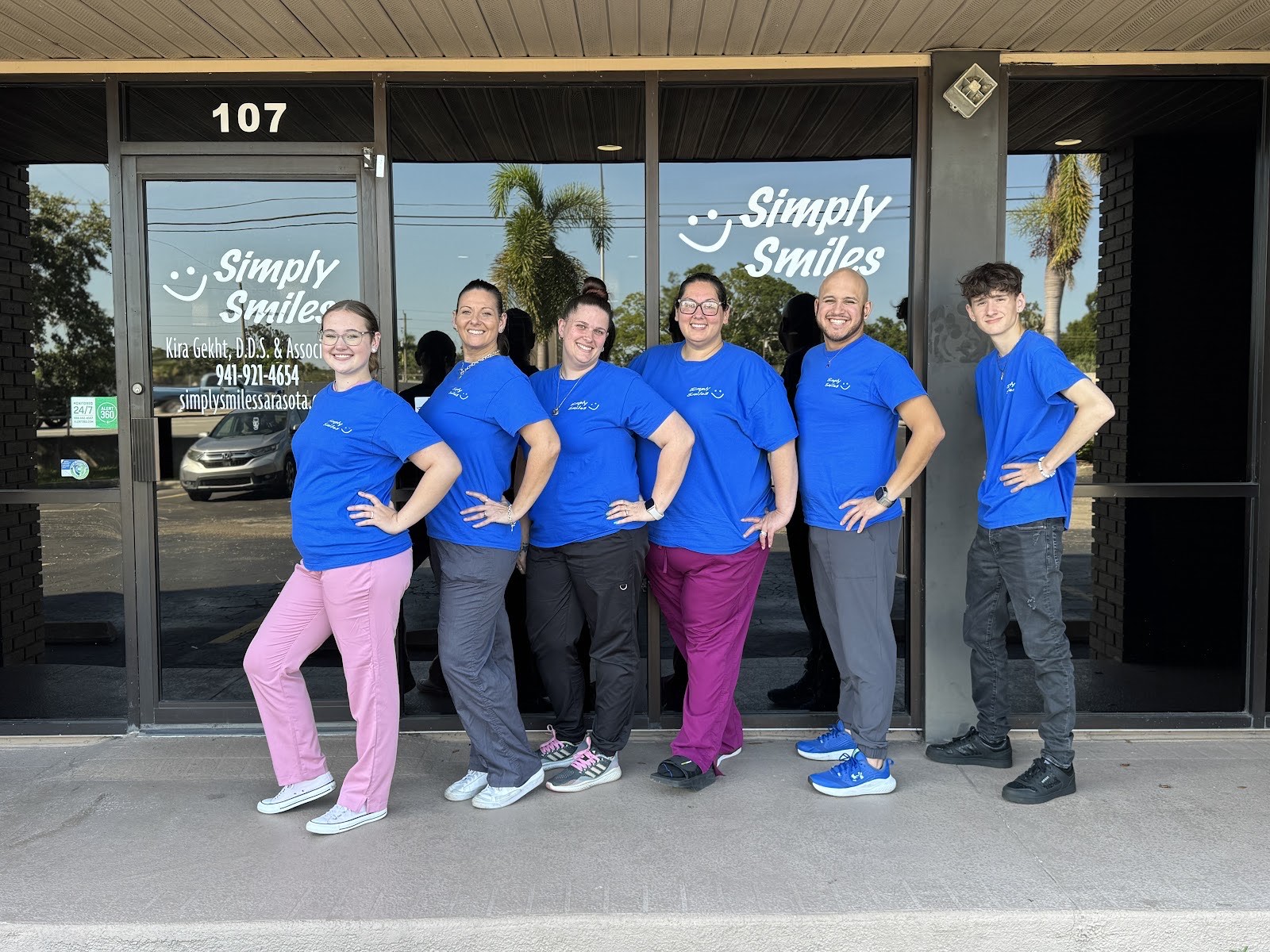 The smiling Simply Smiles team in matching blue shirts outside their Sarasota office at suite 107 on Stickney Point Road