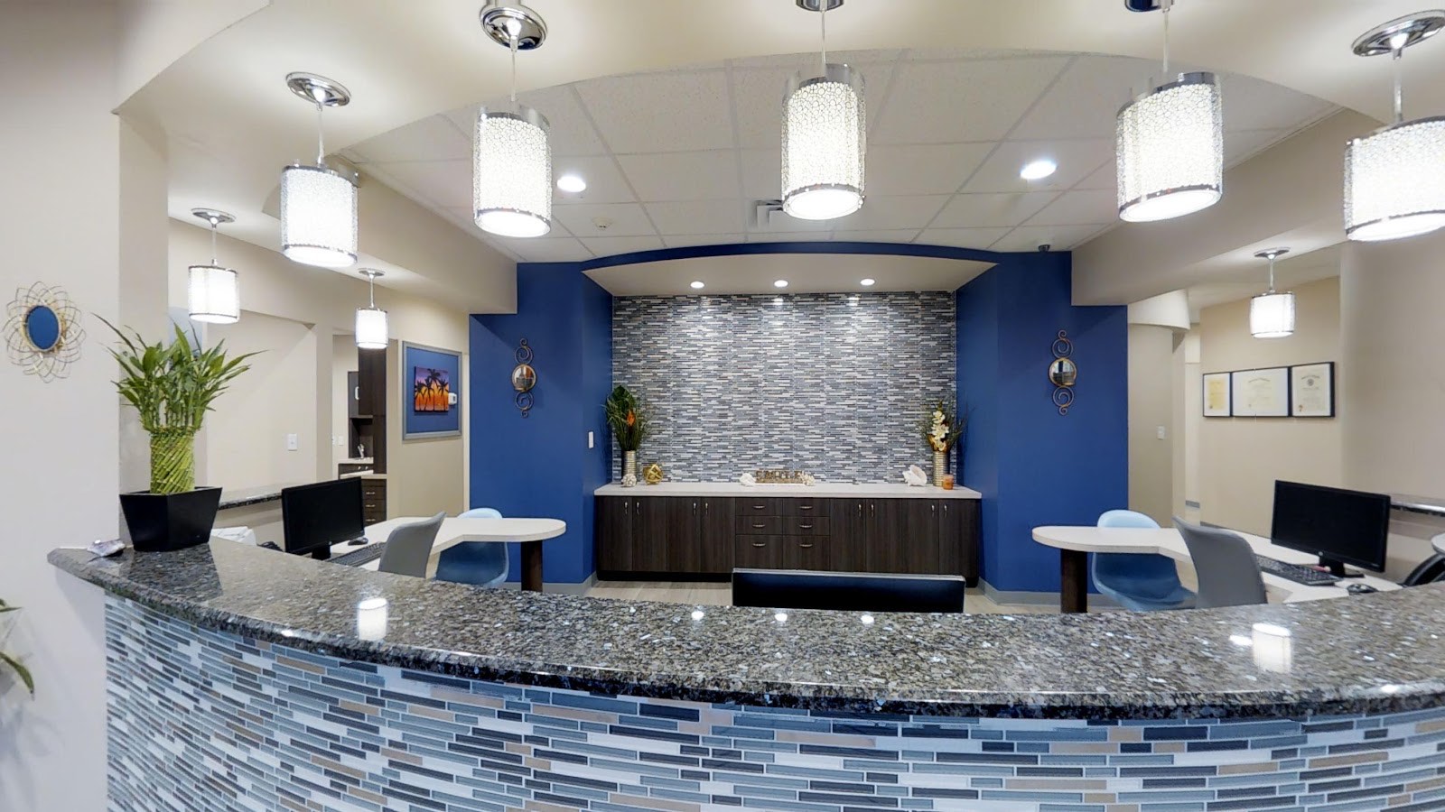 The bright, modern reception lobby at Simply Smiles in Sarasota, with a curved blue mosaic-tile welcome desk and warm pendant lighting