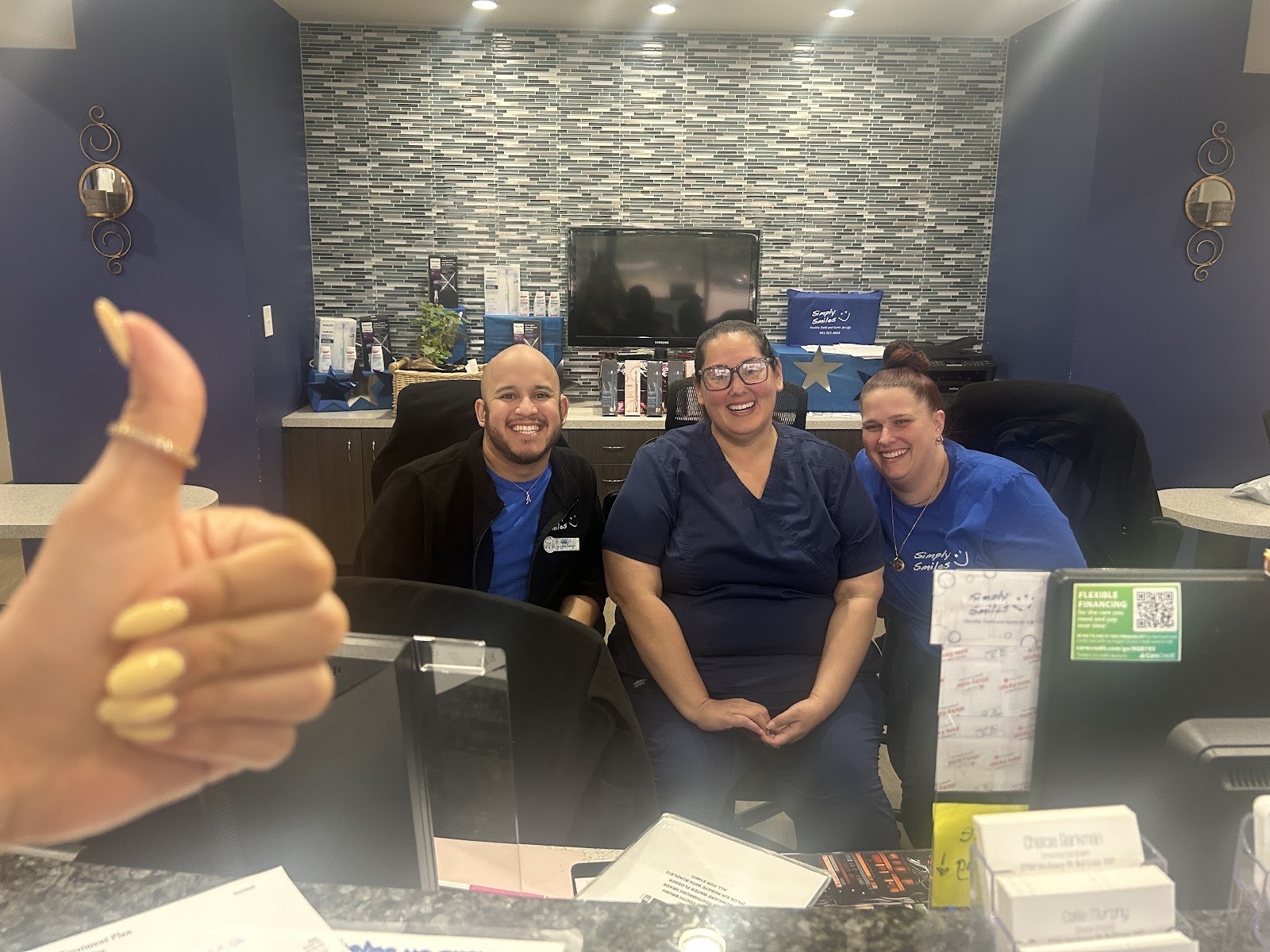 Three smiling Simply Smiles front-desk team members giving a thumbs up behind the welcome counter